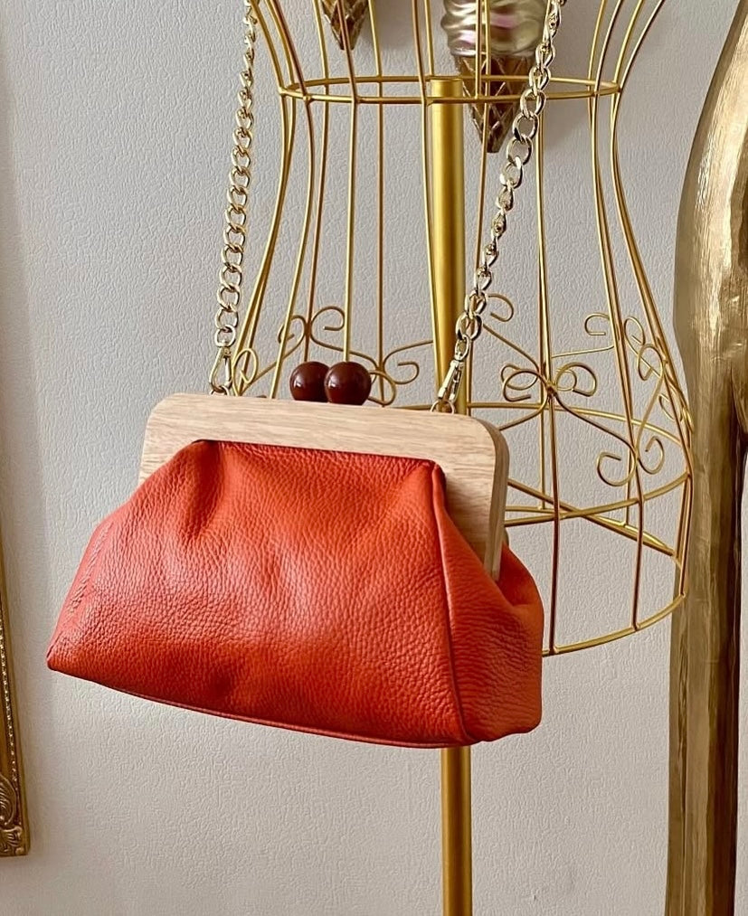 orangene Lederhandtasche mit echtholz Klickverschluss und zwei braunen Holzknöpfen. Goldfarbener Tragegurt/Gliederkette